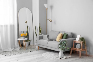 Oturma odasının şık bir iç mekanı. Kanepesi ve ışık duvarının yanında büyük bir ayna.