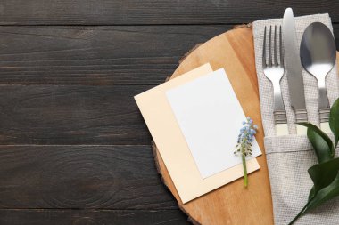 Karanlık ahşap arka planda boş kart, çatal bıçak takımı ve çiçek dekoru.