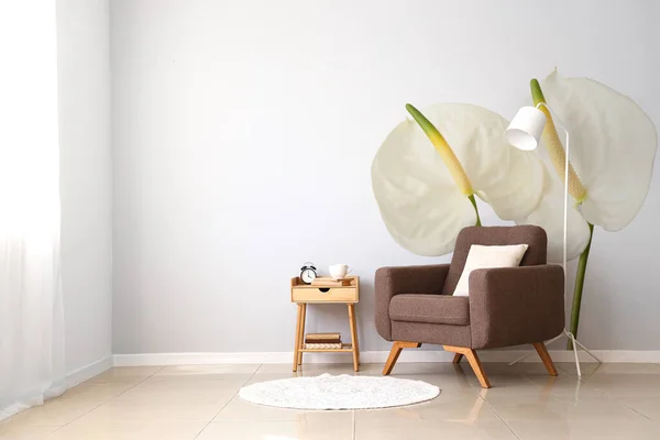 Soft armchair, lamp and table near light wall with print of beautiful flowers