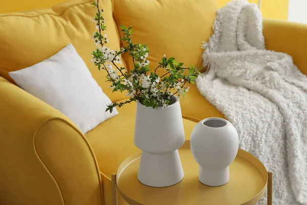 Rahat kanepenin yanındaki masada çiçek açan ağaç dalları olan vazolar.