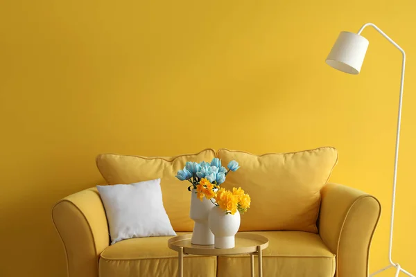 Comfortable sofa and beautiful flowers in colors of Ukrainian flag  on table near color wall in living room