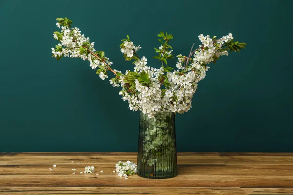 Yeşil duvarın yanındaki ahşap masada güzel ağaç dalları olan vazo.