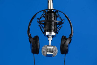 Microphone and headphones on blue background, closeup