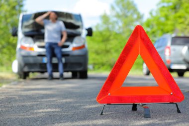 Acil dur işareti ve dışarıdaki kırık arabanın yanında stresli bir adam var.