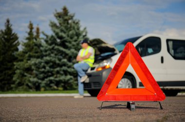 Acil dur işareti ve dışarıdaki kırık arabanın yanında stresli bir adam var.