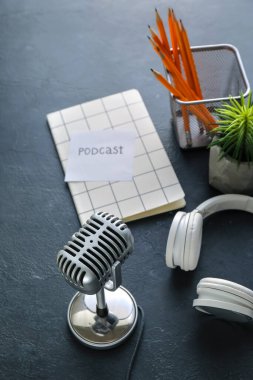 Koyu arkaplanda PODCAST sözcüğü olan mikrofon, kulaklık ve kağıt.