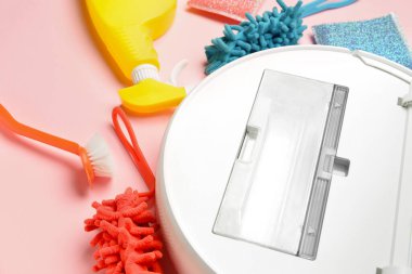 Temizlik malzemeleri seti ve pembe arka planda robot elektrikli süpürge, yakın plan.