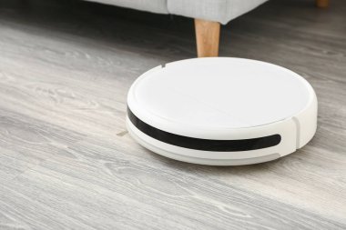 Odanın ahşap zemininde modern robot elektrikli süpürge.