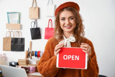 Female business owner holding plate with word OPEN in shop