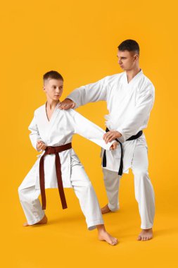 Çocuk sarı arka planda eğitmenle karate çalışıyor.