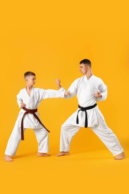 Çocuk sarı arka planda eğitmenle karate çalışıyor.