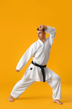 Adam sarı arka planda karate yapıyor.