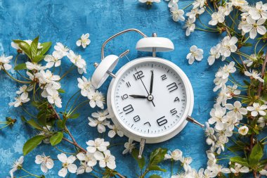 Mavi arka planda açan bahar dalları ve alarm saati, üst görünüm