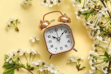Açık renk arkaplan üzerinde çiçek açan bahar dalları ve alarm saati, üst görünüm