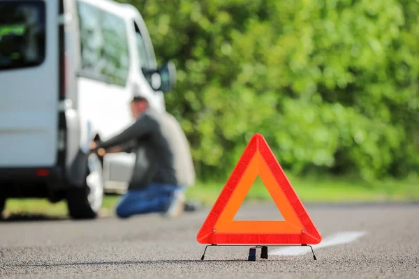 Red emergency triangle stop sign, broken car and man on roadside