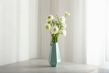 Masada bir buket güzel ranunculus çiçeği olan vazo.