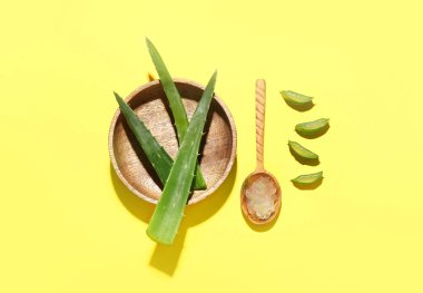Taze kesilmiş aloe vera yapraklı ahşap tabak ve sarı arka planda jöleli kaşık.