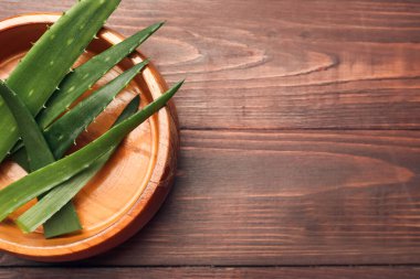 Ahşap arka planda taze aloe yaprakları olan bir kase.