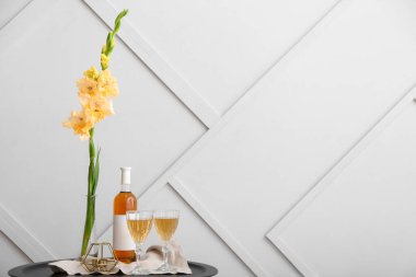 Güzel gladiolus çiçekleri, bardaklar ve şarap şişesi ışık duvarının yanındaki masada.
