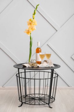 Güzel gladiolus çiçekleri, bardaklar ve şarap şişesi ışık duvarının yanındaki masada.