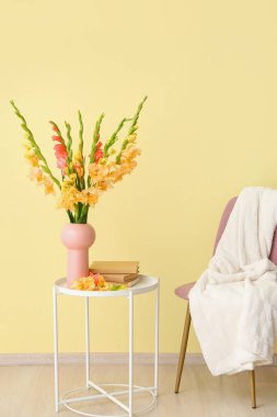 Güzel gladiolus çiçekli vazo ve renkli duvarın yanındaki masada kitaplar.