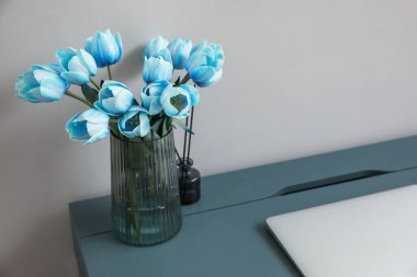Mavi laleli vazo ve gri duvarın yanındaki masada sazlık ayırıcı.