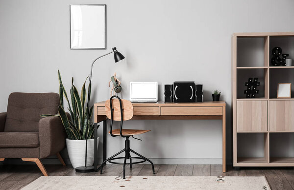 Stylish interior with comfortable workplace, modern laptop and speakers near light wall
