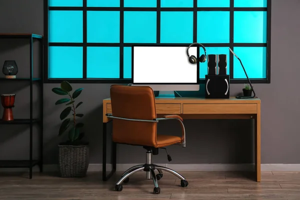 Modern computer, headphones and speakers on table near grey wall