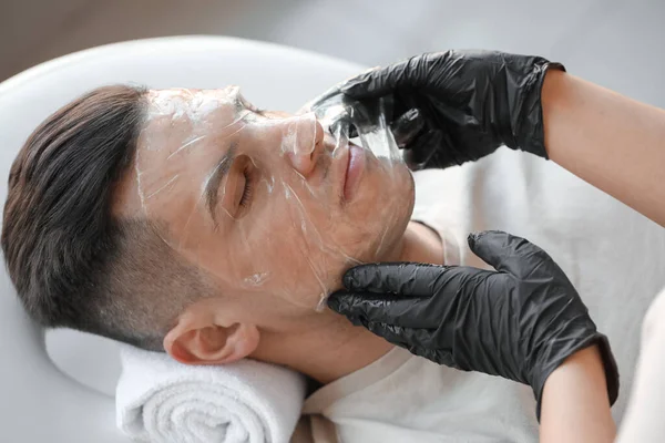 美容师在沙龙 特写镜头中 在年轻人的脸上涂上凝胶面罩 — 图库照片