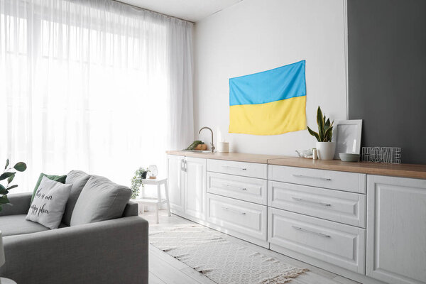 Interior of light kitchen with hanging Ukrainian flag, counters and sofa