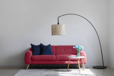 Oturma odasının içinde rahat bir kanepe, yer lambası ve ışık duvarının yanındaki masa.