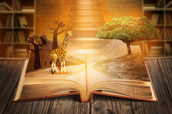 Open magic book with growing tree and giraffe on wooden table in library