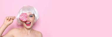 Happy young woman in white wig and with sweet lollipop on light pink background with space for text
