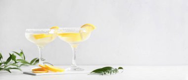 Glasses of tasty martini cocktail with lemon on light background with space for text