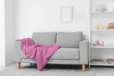 Oturma odasındaki beyaz duvarın yanında ekose ve raf üniteli gri kanepe.