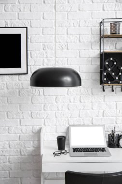 Bilgisayarlı iş yeri, beyaz tuğla duvarın yanındaki masada bir fincan kahve ve gözlük.