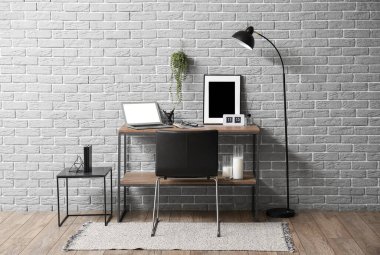 Gri tuğla duvarın yanında dizüstü bilgisayarı, çalar saati ve zemin lambası olan modern işyeri