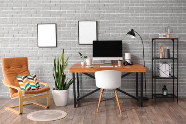 Interior of stylish room with modern workplace and blank photo frames on grey brick wall