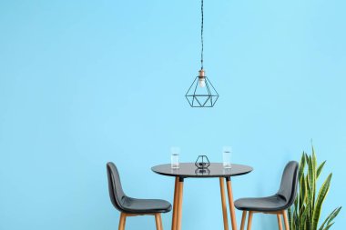 Masada su bardakları, sandalyeler ve renkli duvarın yanında modern lambalar.