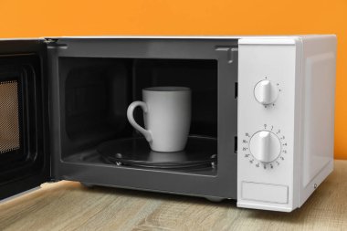 Çağdaş mikrodalga fırında, ahşap masada içkili bir fincan.