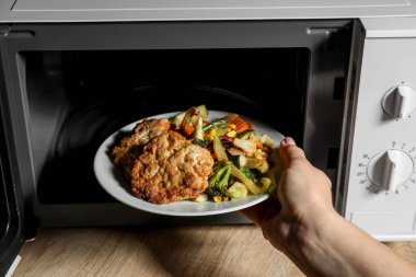 Ahşap masadaki mikrodalga fırına lezzetli yemekler koyan bir kadın.