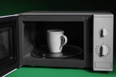 Yeşil arka planda mikrodalga fırında içilen bardak.