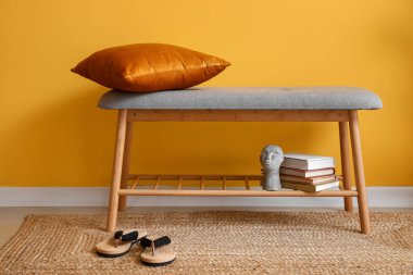 Yastıklı, kitaplı ve sarı duvarlı rahat bir bank.