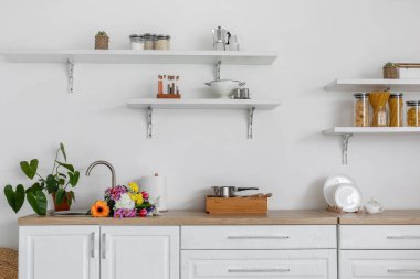 Lavaboda çiçek demeti olan modern aydınlık mutfak.