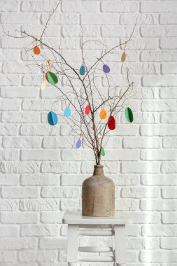 Ağaç dallı vazo ve beyaz tuğla duvarın yanındaki taburede Paskalya dekoru.