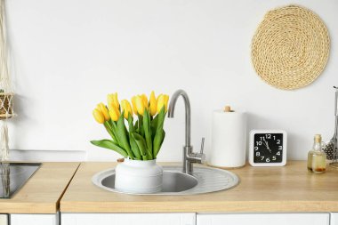 Farklı aletler, alarm saati ve beyaz duvarın yanındaki lavaboda laleler.