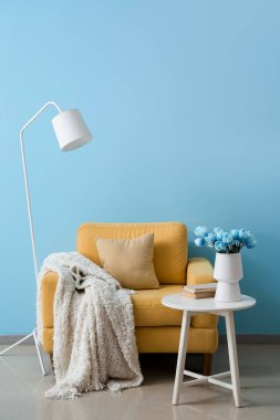 Vazoda laleler, kitaplar, koltuk ve lamba olan masa mavi duvarın yanında.