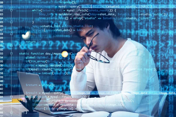 Double exposure of thoughtful male Asian programmer at workplace and computer code