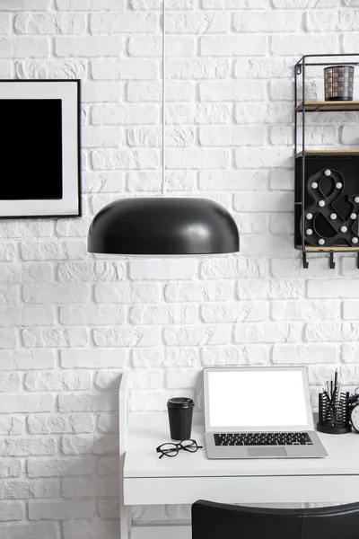 Bilgisayarlı iş yeri, beyaz tuğla duvarın yanındaki masada bir fincan kahve ve gözlük.