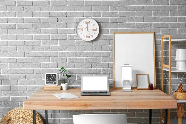 Modern dizüstü bilgisayarı, tablet bilgisayarı ve gri tuğla duvarın yanındaki boş fotoğraf çerçeveleri olan işyeri